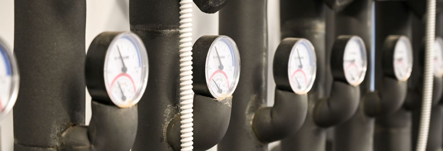 Waagerechte gedämmte Heizungsleitungen mit runden Thermometern in einem Technikraum